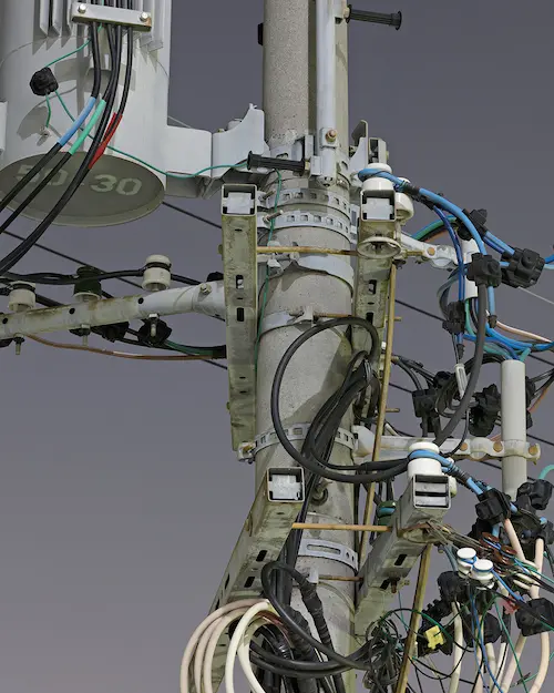 a photo of a power line from a city. the photo is zoomed in on the part where the cables come out of the pole. there is a lot of cables, rods, supports, and other metal pieces present